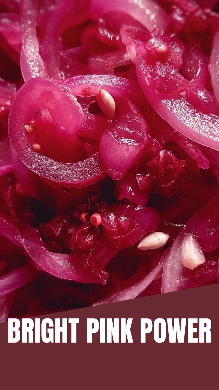 Vibrant pickled red onions in a clear glass jar.